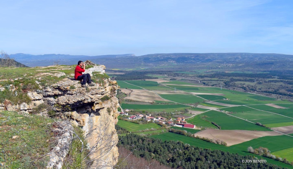 Una persona sentada en el monte Hozalla observa con prismáticos el paisaje 
