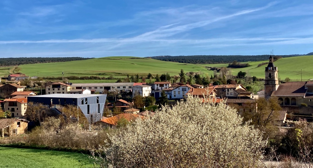 Vista del pueblo de Bóveda con campos verdes al fondo y cielo azul